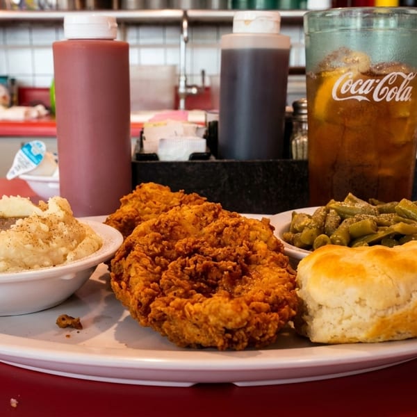A plate of fried chicken, mashed potatoes with gravy, green beans, and a biscuit on a red diner counter.