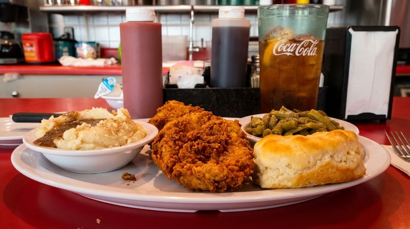 Fried chicken, mashed potatoes with gravy, green beans, biscuit, and a Coca-Cola on a red diner counter.